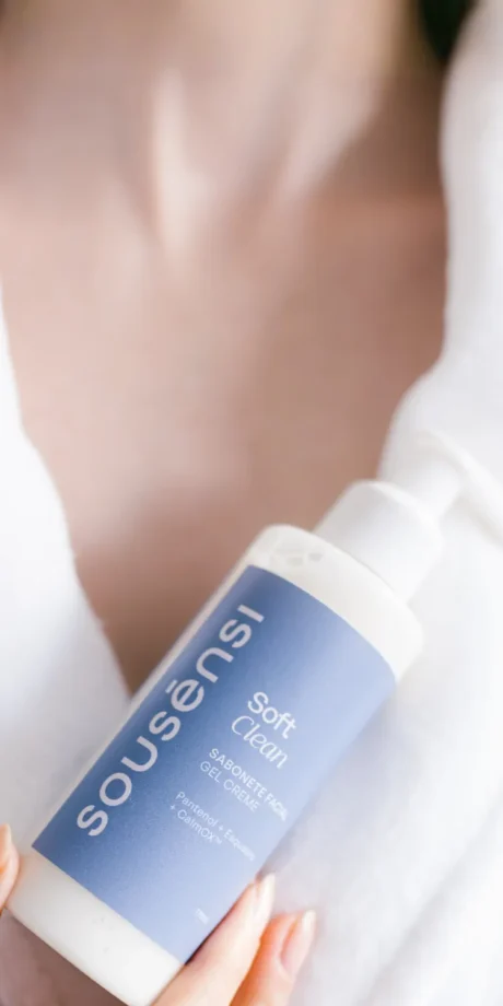 Mão segurando o sabonete facial Soft Clean Sousènsi, frasco com válvula pump, sobre roupão branco